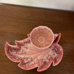 Pu&ograve; includere: Un piatto da portata in ceramica a forma di foglia rosa con una tazza rosa abbinata al centro. Il piatto ha un design marmoreo con vortici bianchi e rosa.