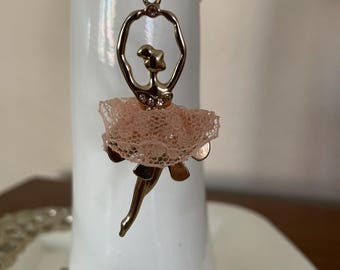 May include: Gold chain necklace with a ballerina pendant. The ballerina is wearing a peach-colored tulle skirt and has rhinestones on her dress.