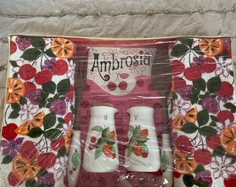 May include: A set of kitchen towels and salt and pepper shakers in a clear plastic package. The towels have a red, orange, and green floral pattern with cherries. The shakers are white ceramic with a cherry and leaf design. The package has the word "Ambrosia" printed on it.