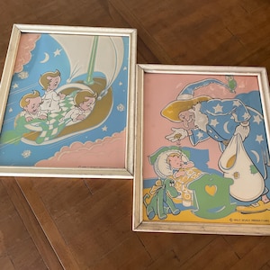 Puede incluir: Dos ilustraciones vintage enmarcadas con personajes de Walt Disney Productions. La primera imagen muestra a tres niños en pijama volando en un velero a través de las nubes. La segunda imagen muestra a un mago rociando polvo mágico sobre un bebé dormido.