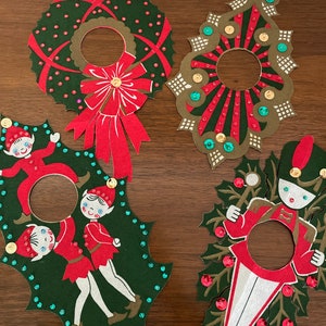 May include: Four vintage Christmas ornaments with a hole in the center for hanging. The ornaments are made of paper and decorated with glitter, sequins, and red, green, and gold colors. One ornament features a wreath, another a Christmas tree, another two elves, and the last a toy soldier.