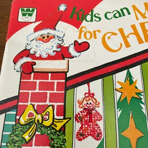 Peut inclure: Une couverture de livre pour enfants vintage avec une illustration rouge et blanche du P&egrave;re No&euml;l qui regarde par une chemin&eacute;e. Le titre du livre est "Kids can Make for Christmas" en lettres vertes et orange.