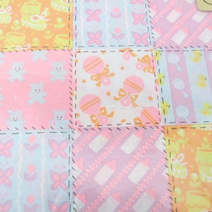 May include: A patchwork fabric with a variety of pastel colors and patterns, including baby animals, flowers, and toys. The fabric is perfect for quilting, sewing, or crafting.