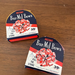 May include: Two boxes of Bur-Mil Bows, featuring a red and white bow illustration. The boxes have a navy blue background with the text "INSTANT Bur-Mil Bows" and "JUST PULL THE STRING". Each box contains 15 feet of ribbon.