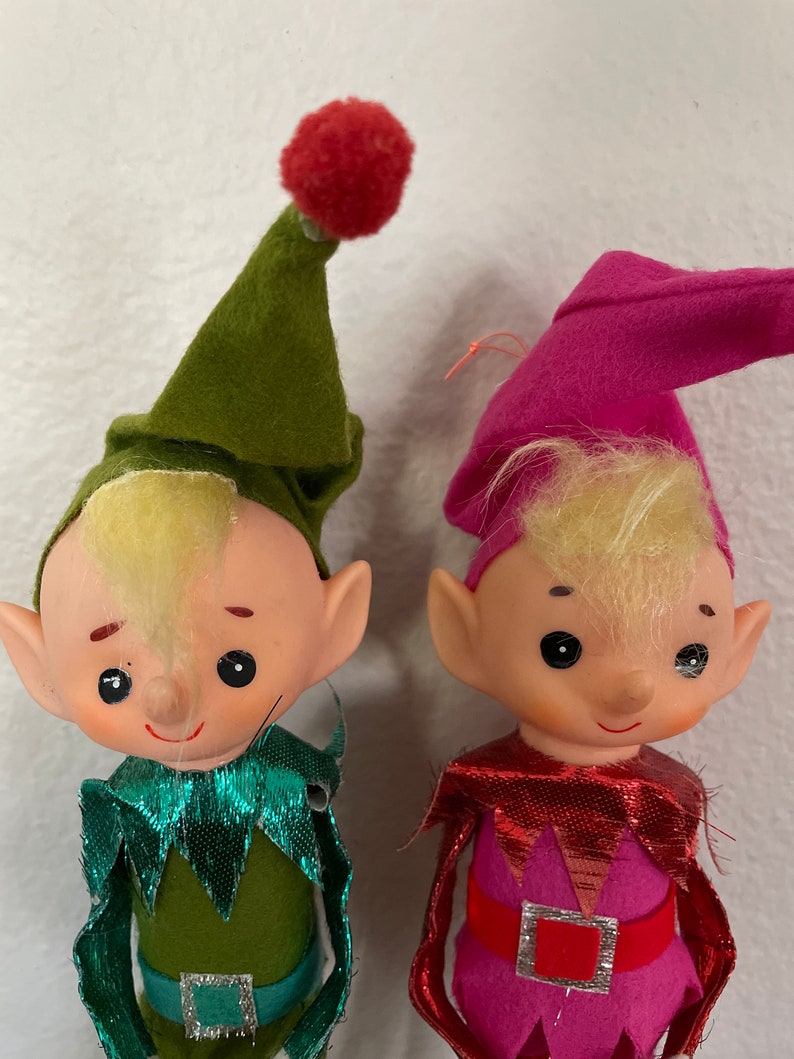 May include: Two vintage felt Christmas elves with green and pink hats, blonde yarn hair, and sparkly green and red collars.