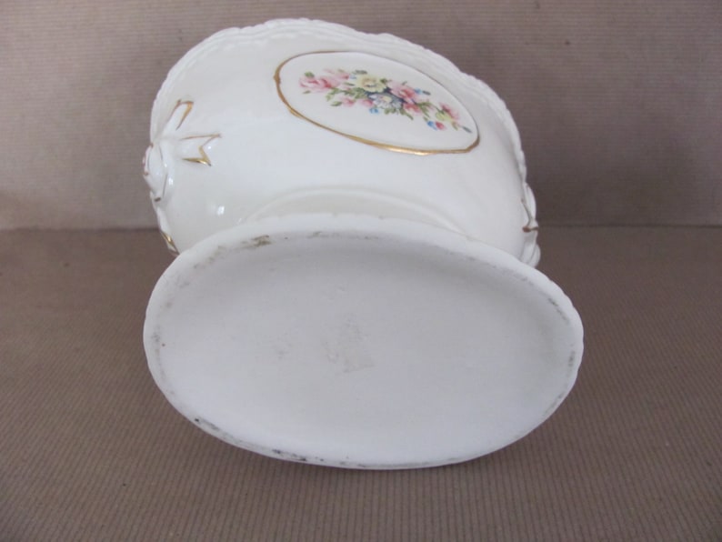 Puede incluir: Jarr&oacute;n de cer&aacute;mica blanca con un dise&ntilde;o floral y detalles dorados. El jarr&oacute;n tiene una base redonda y una abertura ancha.