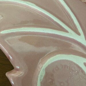 Pu&ograve; includere: Un piatto in ceramica rosa con un design bianco. Il piatto ha un bordo ondulato e un design in rilievo al centro. Il fondo del piatto ha un cerchio bianco con le parole "Made in Japan" stampate in nero.