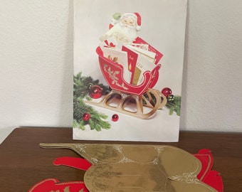 Op de afbeelding: Een Hallmark Plans-a-Party kaarthouder met een rode slee, een Santa-beeldje en kaarten. De verpakking leest "Sleigh" en is 22.86 cm hoog. Extra gouden en rode slee-uitsparingen zijn zichtbaar.