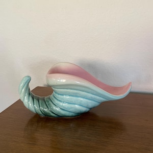 May include: A ceramic cornucopia planter in shades of pink, blue, and green. The planter is shaped like a horn with a curled end.