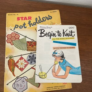 May include: Two vintage craft books on a wooden surface. The larger book, "Star Pot Holders," has a yellow cover with illustrations of pot holders. The smaller book, "Begin to Knit," features a woman knitting. Both books are from American Thread Company.