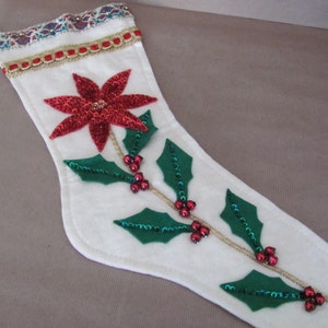 May include: White Christmas stocking with a red poinsettia and green holly leaves with red berries.