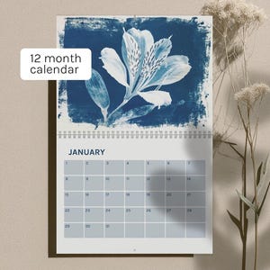Könnte beinhalten: Ein 12-Monats-Kalender mit einem blau-weißen Blumendesign. Der Kalender zeigt den Monat Januar mit einem Raster von Daten. Der Text "12 month calendar" befindet sich in einem weißen Feld oben links.
