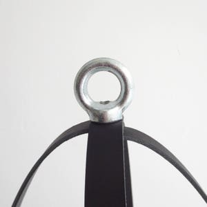 May include: A black leather hanging planter with a silver metal ring at the top. The planter is made of three leather straps that form a sphere.