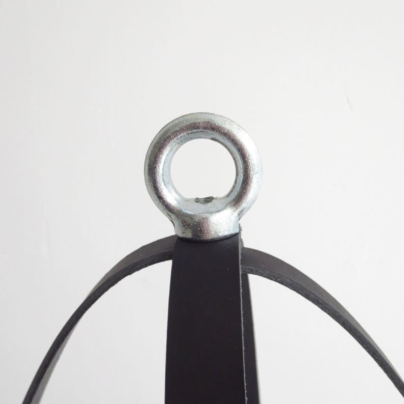 May include: A black leather hanging planter with a silver metal ring at the top. The planter is made of three leather straps that form a sphere.