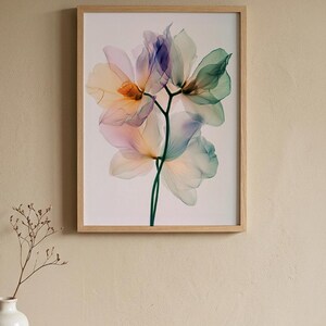 May include: A framed floral print featuring a close-up of translucent flowers in shades of peach, purple, and green. The artwork is set against a white background and framed in light wood. The image is mounted on a beige wall.