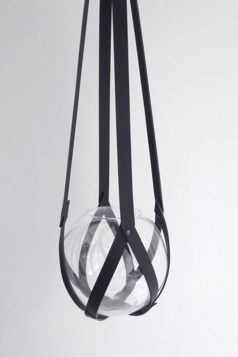 May include: A black leather hanging planter with a clear glass globe. The leather straps are woven together to create a sturdy and stylish design.