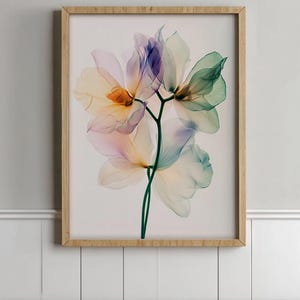 May include: A framed floral art print featuring translucent flowers in shades of purple, green, and yellow. The artwork is set against a white background and framed in a light-colored wooden frame. The flowers are detailed and delicate.