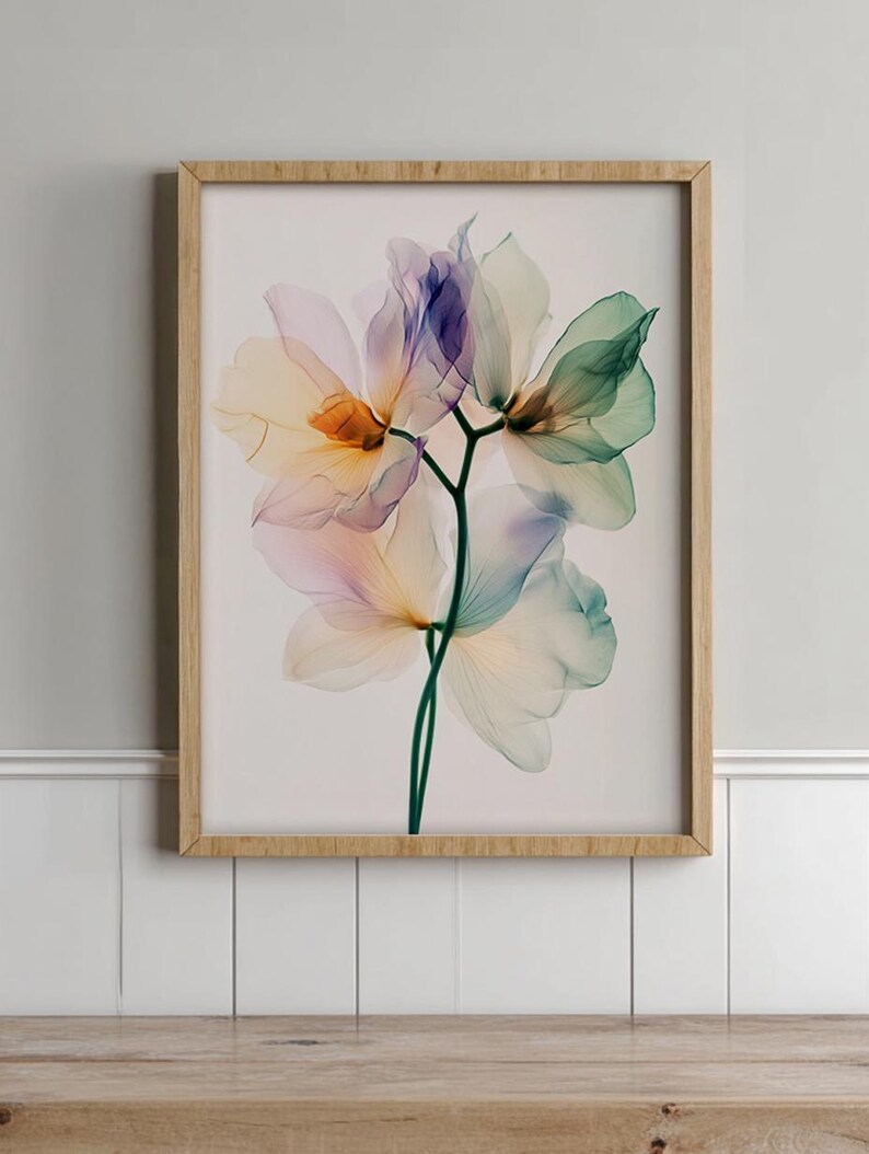 May include: A framed floral art print featuring translucent flowers in shades of purple, green, and yellow. The artwork is set against a white background and framed in a light-colored wooden frame. The flowers are detailed and delicate.