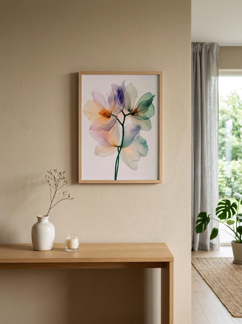 May include: A framed floral print featuring translucent flowers in shades of peach, blue, and green. The artwork is displayed on a beige wall above a wooden table. A white vase with a sprig and a candle are on the table.