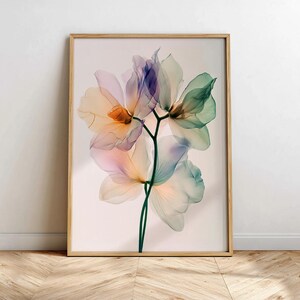 May include: A framed art print featuring a close-up of delicate, translucent flowers in shades of peach, purple, and green. The botanical illustration is set against a soft, neutral background, encased in a light wood frame.