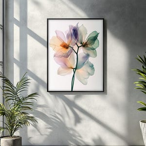 May include: A framed art print featuring a close-up of delicate, translucent flowers in shades of peach, lavender, and green. The floral arrangement is set against a white background, encased in a black frame, and mounted on a textured wall.