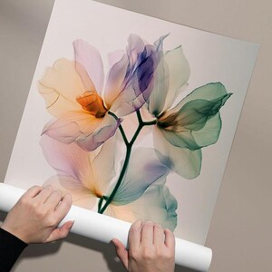 May include: A floral art print featuring translucent flowers in shades of orange, pink, purple, and green. The delicate petals are set against a white background. The print is held by a person.