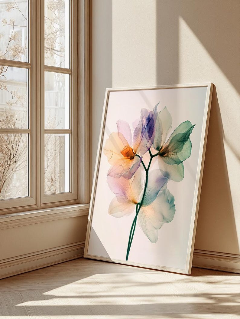 May include: A framed floral art print featuring a delicate, translucent flower with petals in shades of orange, pink, purple, and green. The artwork is set against a neutral background and leans against a wall near a window.