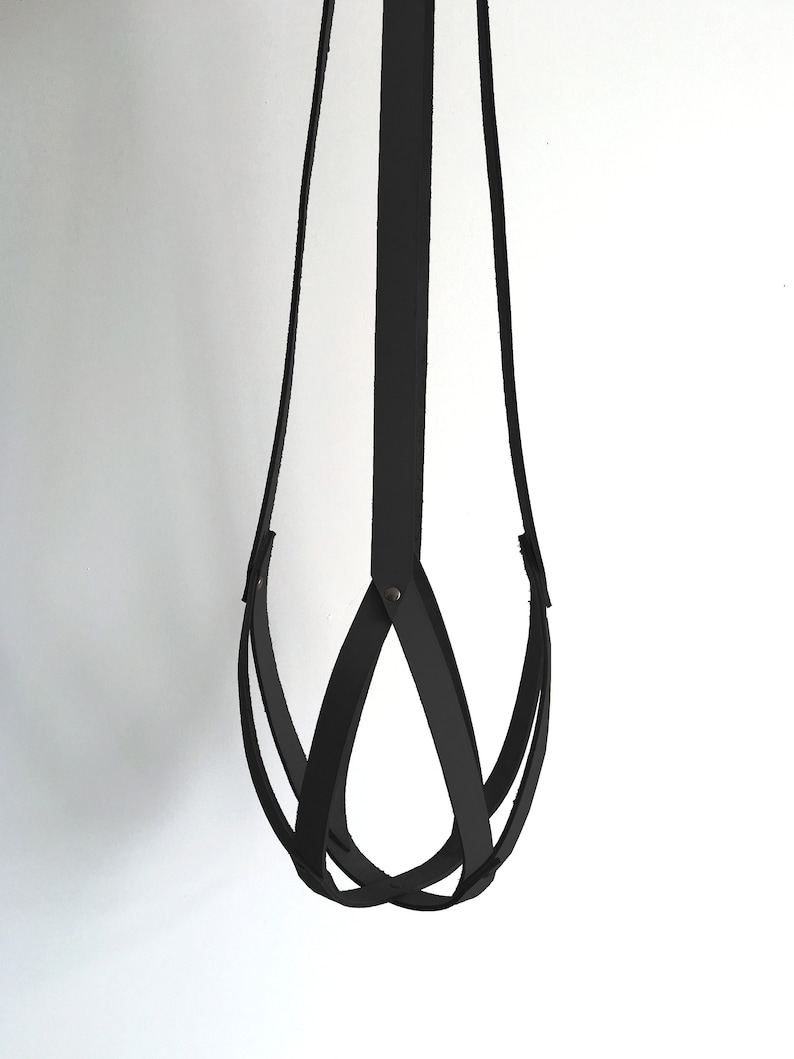May include: A black leather hanging planter with a woven design. The planter is made of multiple strips of leather that are woven together to create a unique and stylish design.
