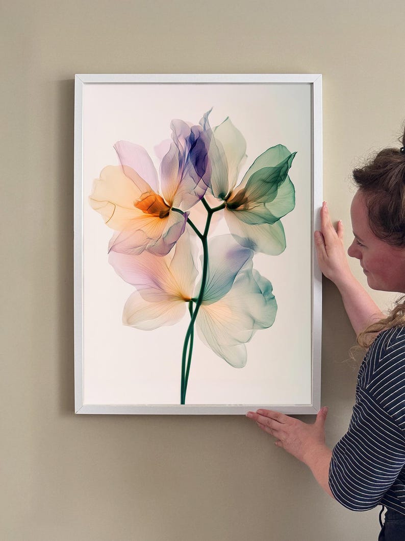 May include: A framed floral art print featuring a translucent flower design. The artwork showcases petals in shades of orange, purple, and green, set against a cream background. The print is encased in a white frame, suitable for home decor.
