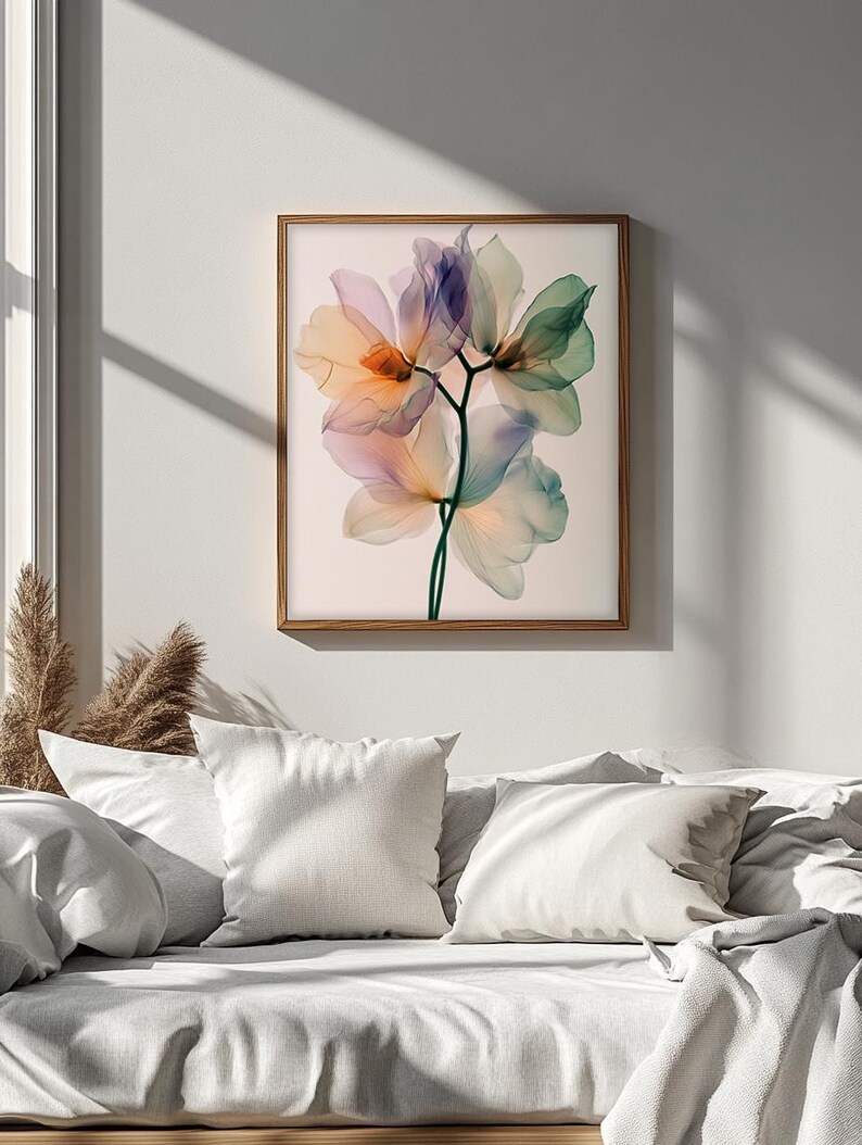 May include: A framed floral art print featuring delicate, translucent flowers in shades of orange, purple, and green. The artwork is set against a light background and framed in a natural wood frame. The print is displayed above a bed with white pillows and bedding.