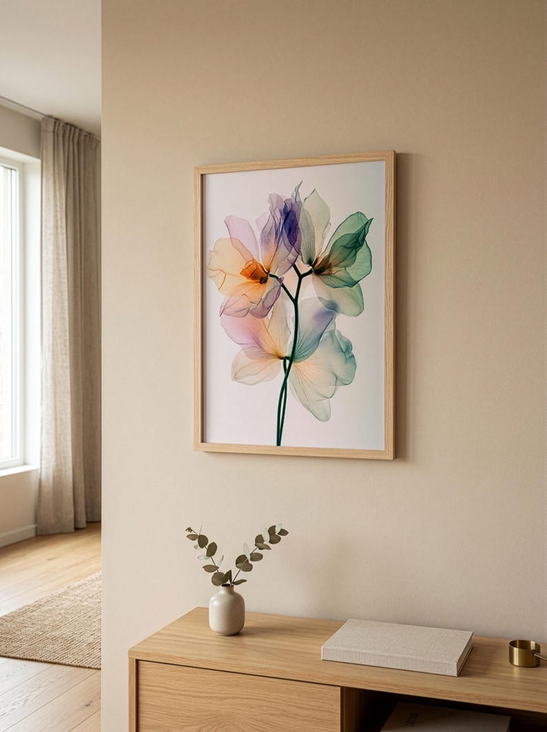 May include: A framed floral art print featuring translucent flowers in shades of purple, orange, green, and blue. The artwork is displayed in a light wood frame and hangs on a beige wall. A small vase with greenery sits on a wooden cabinet below.