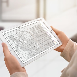 May include: A person is using a tablet to view a cross-stitch pattern. The pattern is displayed on the screen in black and white, with a grid of squares. The tablet is white and has a black bezel.