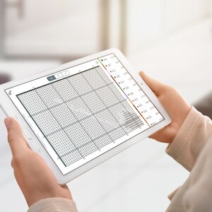 May include: A white tablet displaying a cross-stitch pattern on the screen. The pattern is a grid of small squares, with some squares filled in with different colours. The tablet is being held by a person's hands.