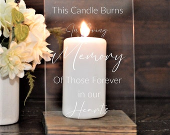 May include: A clear acrylic candle holder with a wooden base. The holder has a white candle inside and the text "This candle burns in loving memory of those forever in our hearts".