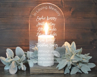 May include: A clear acrylic memorial candle holder with an arch top. The holder has a white candle inside and the text "In Loving Memory" at the top. The names "Sophie Kinney", "Heather May", "Att Taylor", "Aaron Taylor", "Matt Kelboyl", and "Jonathan Yanes" are engraved on the holder. The text "Although you couldn't be here today, you are forever present in our hearts." is also engraved on the holder.