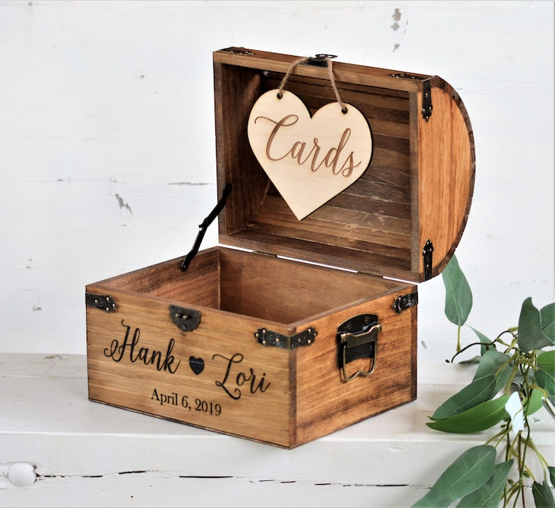 Puede incluir: Un cofre del tesoro de madera con un letrero en forma de coraz&oacute;n que dice "Cards" colgando de la parte superior. El cofre est&aacute; grabado con "Hank & Lori" y la fecha "April 6, 2019".