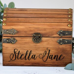 May include: A wooden treasure chest with metal accents and a hinged lid. The chest is engraved with the name "Stella Jane".