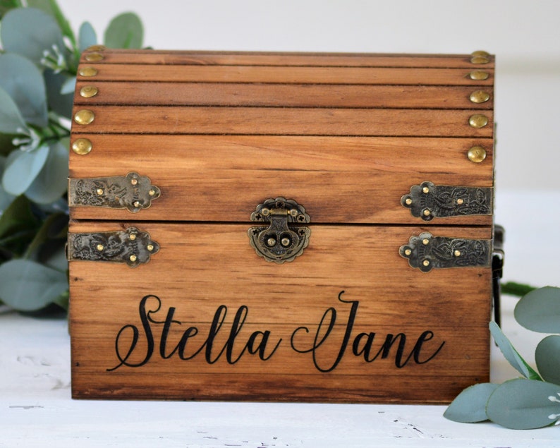 May include: A wooden treasure chest with metal accents and a hinged lid. The chest is engraved with the name "Stella Jane".