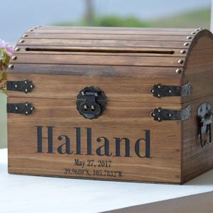 Peut inclure: Un coffre en bois avec un couvercle &agrave; charni&egrave;res et une fente pour les cartes. Le coffre est d&eacute;cor&eacute; d'accents m&eacute;talliques et porte le nom "Halland" grav&eacute; sur le devant, ainsi que la date "May 27, 2017" et des coordonn&eacute;es.