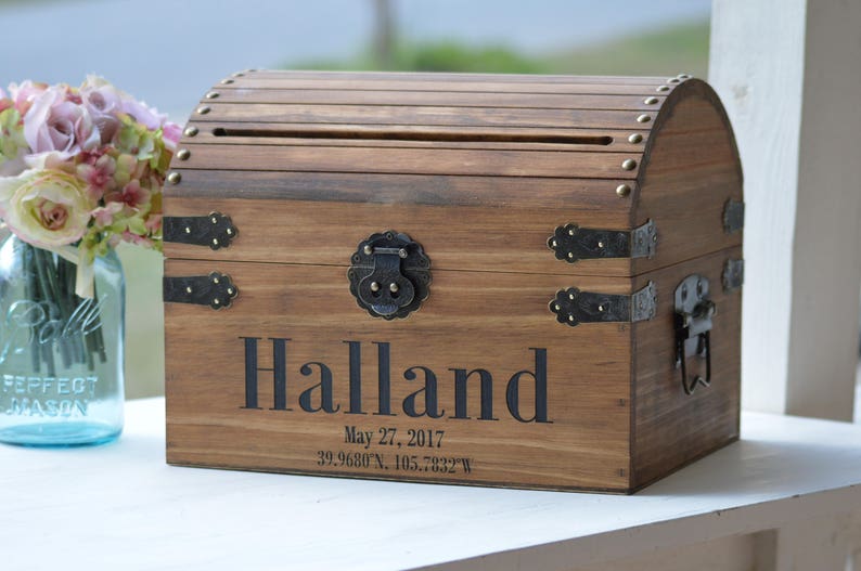 Peut inclure: Un coffre en bois avec un couvercle &agrave; charni&egrave;res et une fente pour les cartes. Le coffre est d&eacute;cor&eacute; d'accents m&eacute;talliques et porte le nom "Halland" grav&eacute; sur le devant, ainsi que la date "May 27, 2017" et des coordonn&eacute;es.