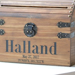 Peut inclure: Coffre en bois avec un couvercle &agrave; charni&egrave;res et des fermoirs en m&eacute;tal. Le coffre est grav&eacute; du nom "Halland" et de la date "27 mai 2017". Le coffre est une bo&icirc;te &agrave; cartes de mariage.