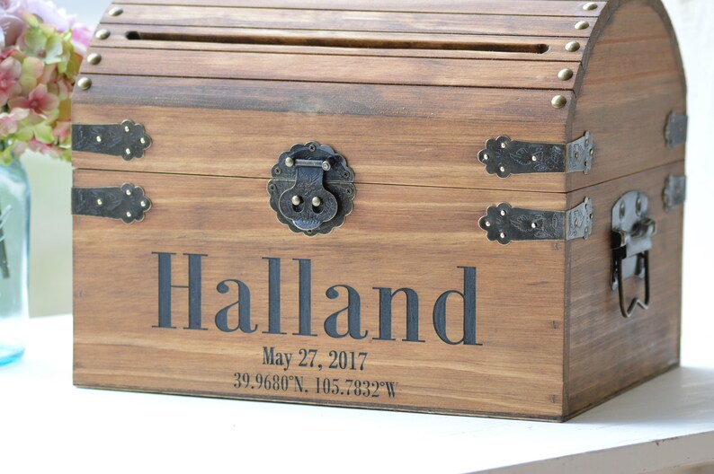 Peut inclure: Coffre en bois avec un couvercle &agrave; charni&egrave;res et des fermoirs en m&eacute;tal. Le coffre est grav&eacute; du nom "Halland" et de la date "27 mai 2017". Le coffre est une bo&icirc;te &agrave; cartes de mariage.