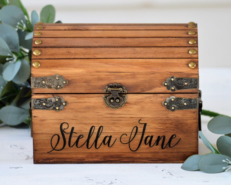 May include: A wooden treasure chest with brass accents and a hinged lid. The chest is engraved with the name "Stella Jane".