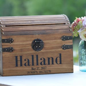 Peut inclure: Un coffre en bois avec une fente sur le dessus pour les cartes ou les lettres. Le coffre est d&eacute;cor&eacute; de ferrures en laiton et porte le nom "Halland" grav&eacute; sur le devant. La date "27 mai 2017" et les coordonn&eacute;es "39.9680&deg;N, 105.7632&deg;W" sont &eacute;galement grav&eacute;es sur le devant.