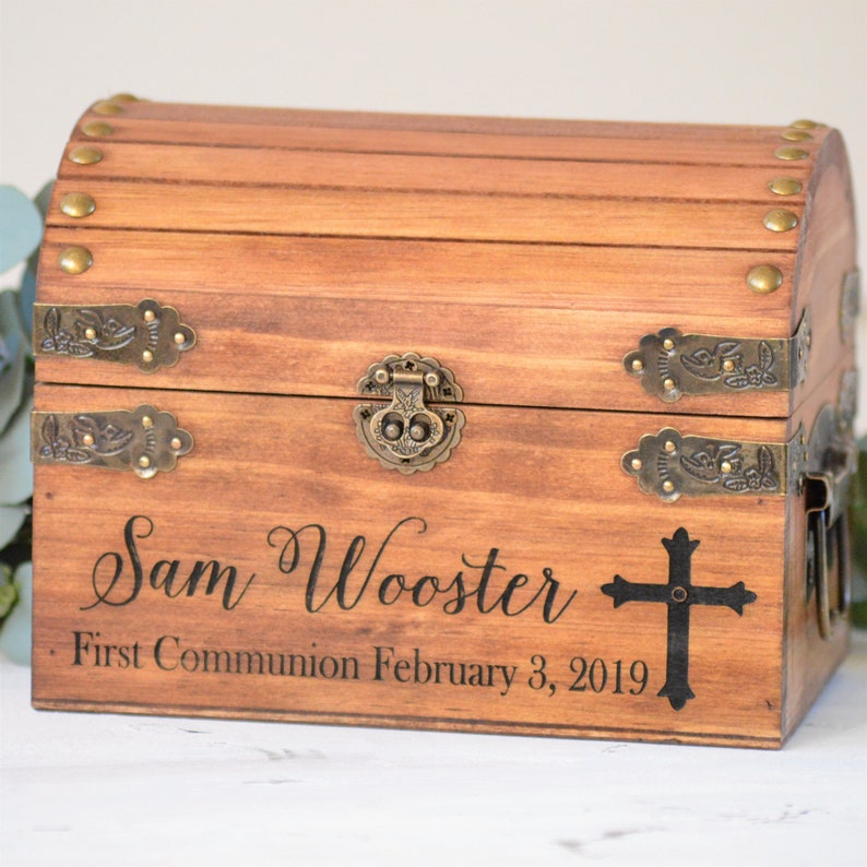 Puede incluir: Un cofre del tesoro de madera con detalles en lat&oacute;n y un dise&ntilde;o de cruz. El cofre est&aacute; grabado con el texto "Sam Wooster First Communion February 3, 2019".