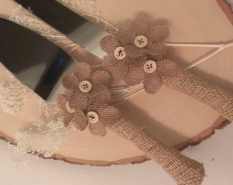 May include: A set of two cake knives with burlap handles and brown fabric flowers with buttons in the center. The knives are on a wooden slice.