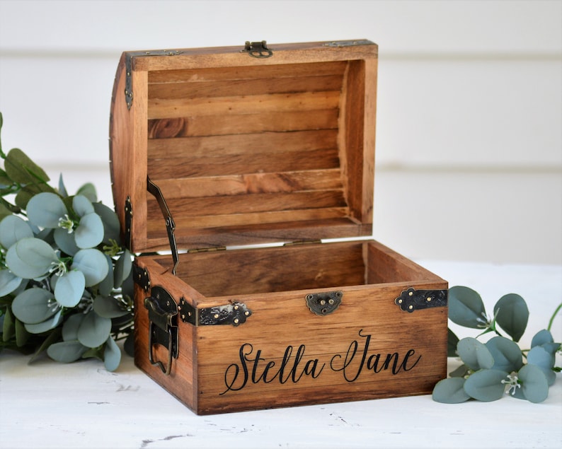 May include: A wooden treasure chest with a hinged lid and metal accents. The chest is open and the inside is empty. The chest is engraved with the name "Stella Jane".