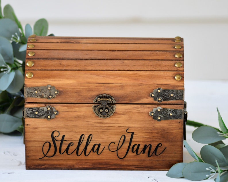 May include: A wooden treasure chest with brass accents and a personalized inscription that reads "Stella Jane".
