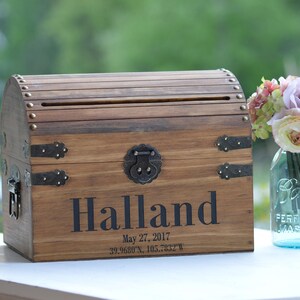 Peut inclure: Coffre en bois avec une fente sur le dessus pour les cartes ou les enveloppes. Le coffre est d&eacute;cor&eacute; d'accents m&eacute;talliques et le nom "Halland" est grav&eacute; sur le devant. La date "27 mai 2017" et les coordonn&eacute;es "39.9680&deg;N, 105.2822&deg;W" sont &eacute;galement grav&eacute;es sur le devant.