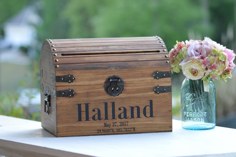 Peut inclure: Coffre en bois avec une fente sur le dessus pour les cartes ou les enveloppes. Le coffre est d&eacute;cor&eacute; d'accents m&eacute;talliques et le nom "Halland" est grav&eacute; sur le devant. La date "27 mai 2017" et les coordonn&eacute;es "39.9680&deg;N, 105.2822&deg;W" sont &eacute;galement grav&eacute;es sur le devant.